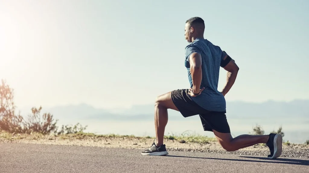Man performing a deep lunge stretch on an open road with a scenic background.